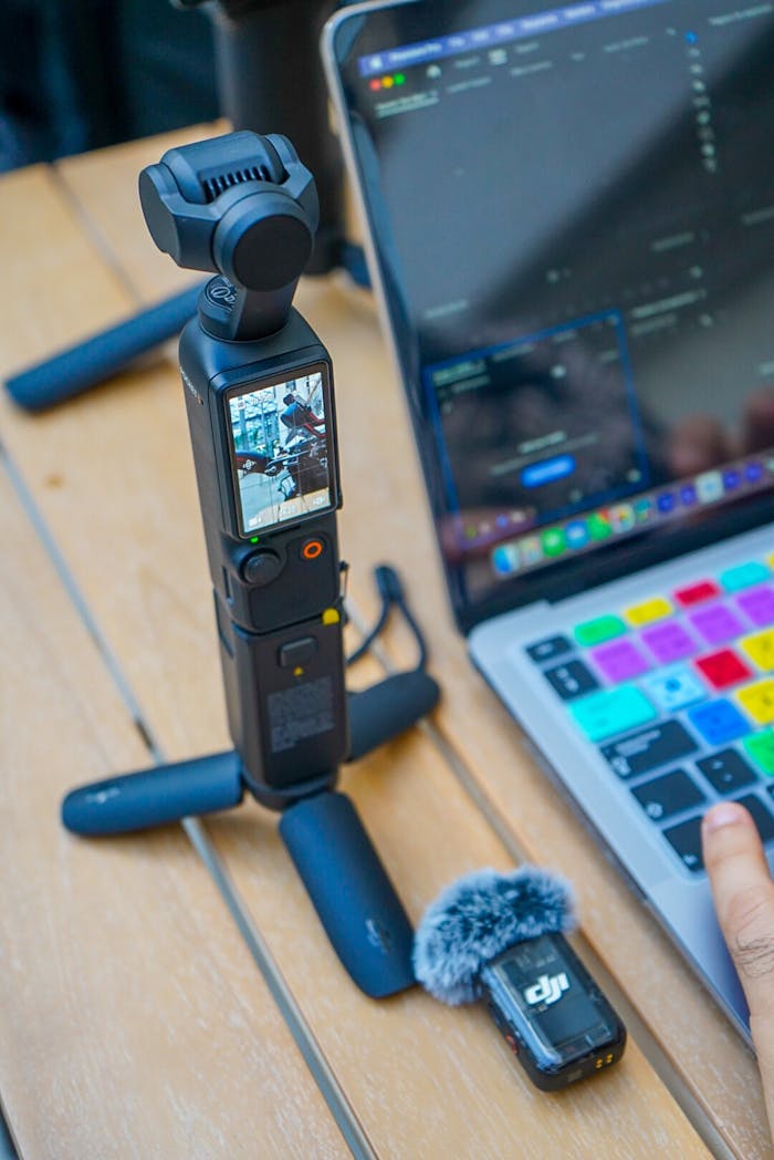 A compact vlogging setup with a camera, laptop, and microphone on a wooden desk, showcasing modern technology.